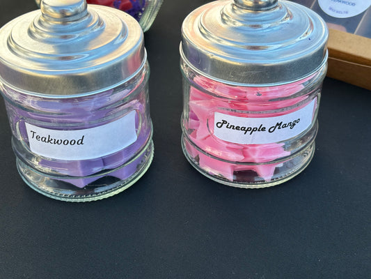 Two small glass jars filled with wax melts. 1 jar fragrance is Pineapple Mango and the 2nd jar fragrance is Watermelon Lemonade. Enjoy the Aroma while it melts down on your wax burner or warmer.